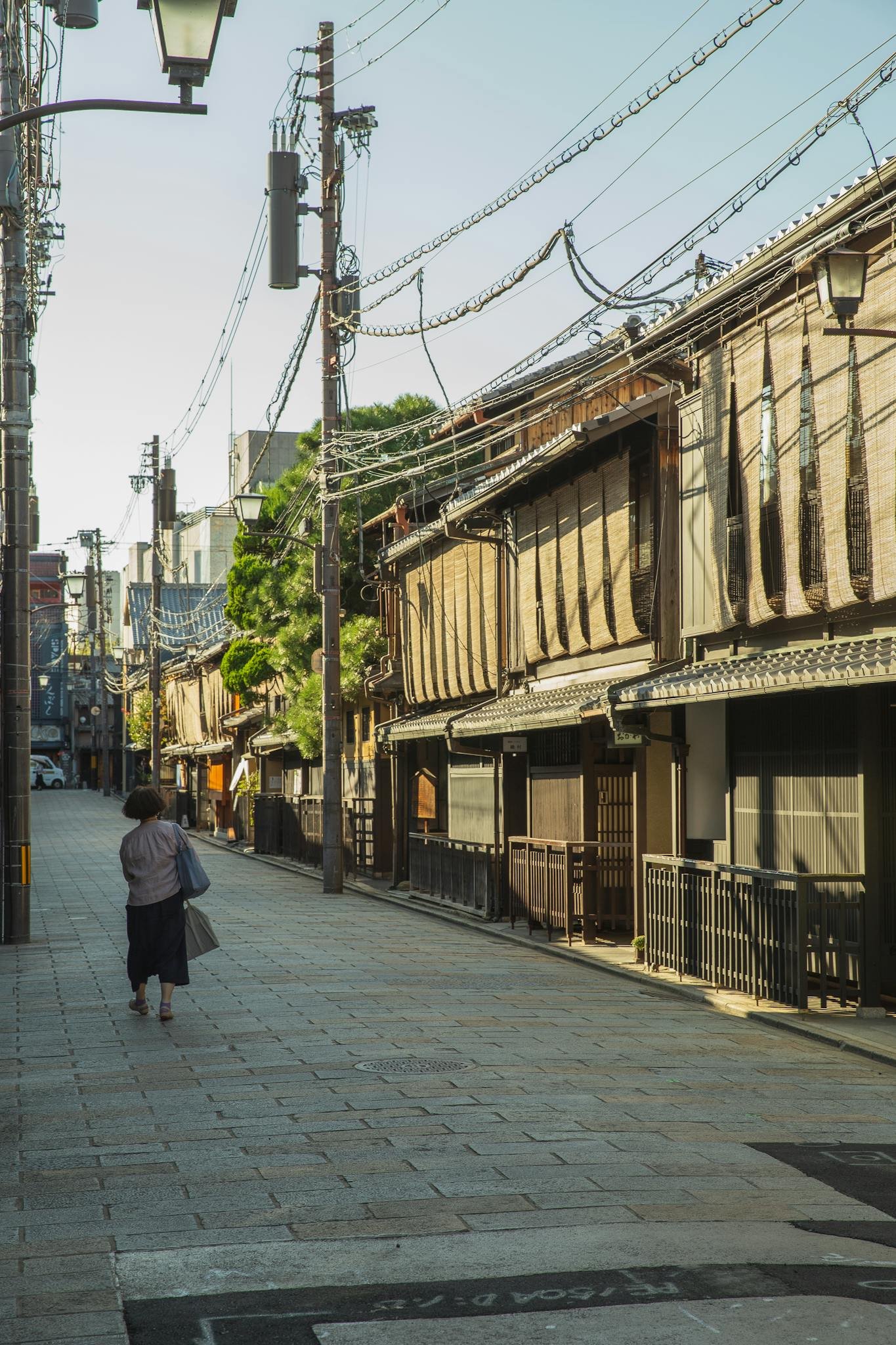 Back view of unrecognizable local female walking on paved street of ancient city district on sunny morning